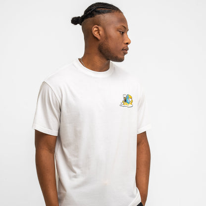 A man with braided hair wears the Guinness Seb Curi Oversize Tee in white from Guinness Webstore US, featuring a small colorful chest graphic, as he stands against a plain white background looking to his left.