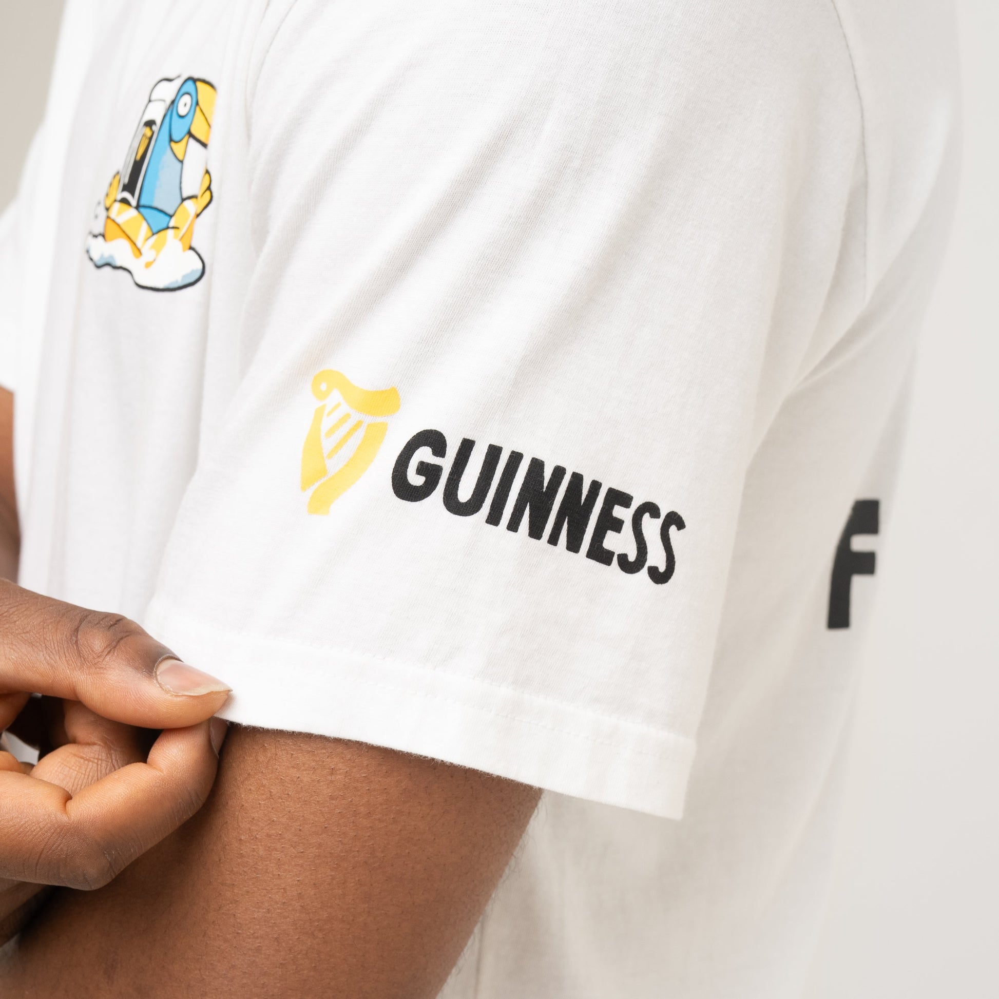 A person adjusts the sleeve of the Guinness Seb Curi Oversize Tee - White, an exclusive from Guinness Webstore US featuring a black and yellow logo on the upper arm.