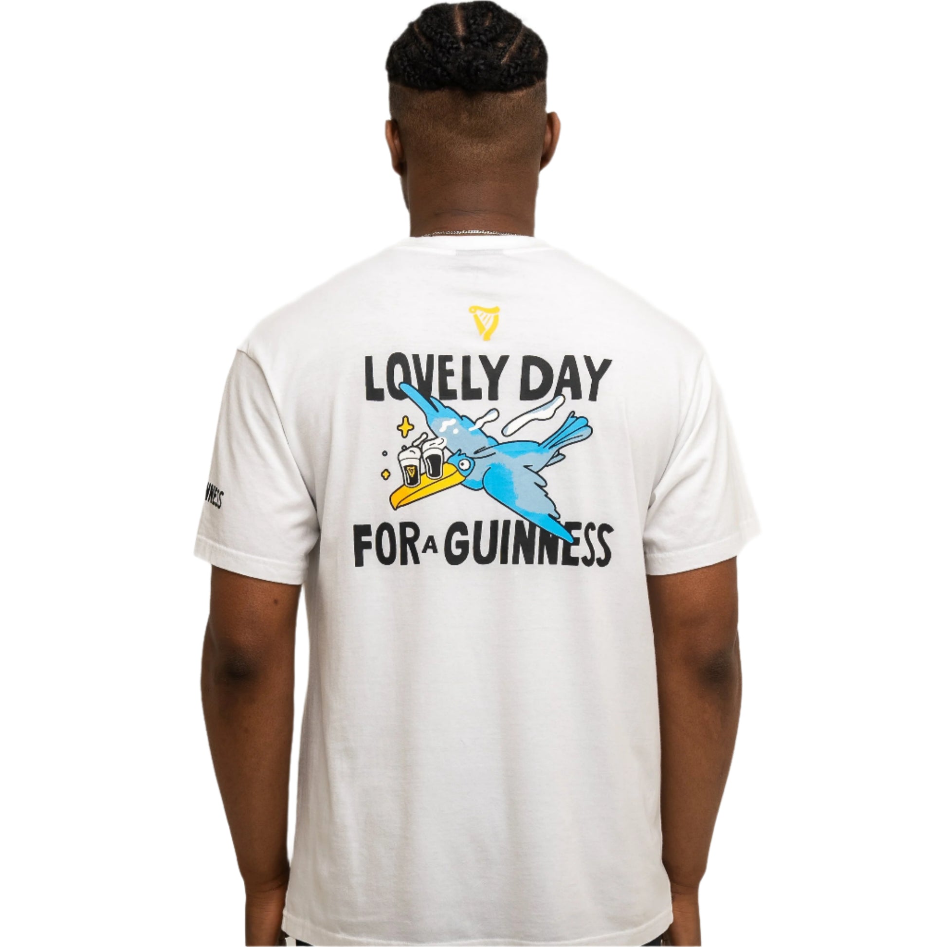 Someone wears the Guinness Seb Curi Oversise Tee - White from Guinness Webstore US, a white T-shirt with a blue bird holding a pint and "Lovely Day for a Guinness" graphic on the back.