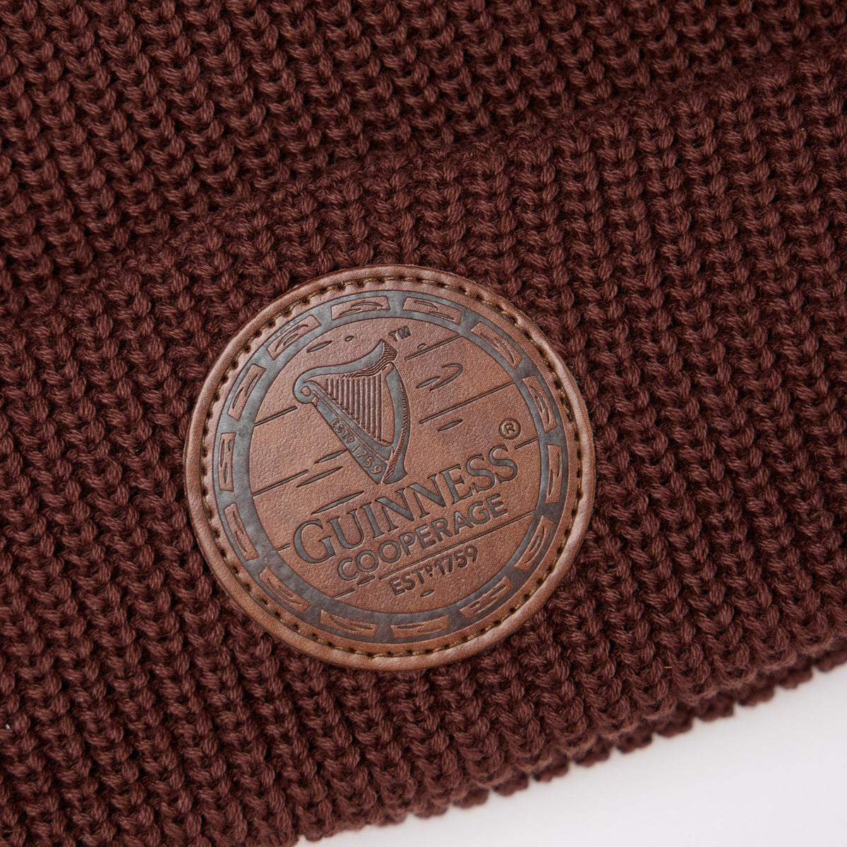 Close-up of the Guinness Cooperage Brown Knitted Beanie with a round leather patch embossed with the cooperage logo and “Guinness Cooperage ESTD 1759” harp design.