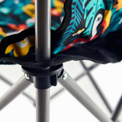 Close-up of the Guinness x Fatti Burke Hawaiian Camping Chair’s metal frame and fabric seat featuring a vibrant toucan and leaf pattern, perfect for pairing with a colorful beach towel.