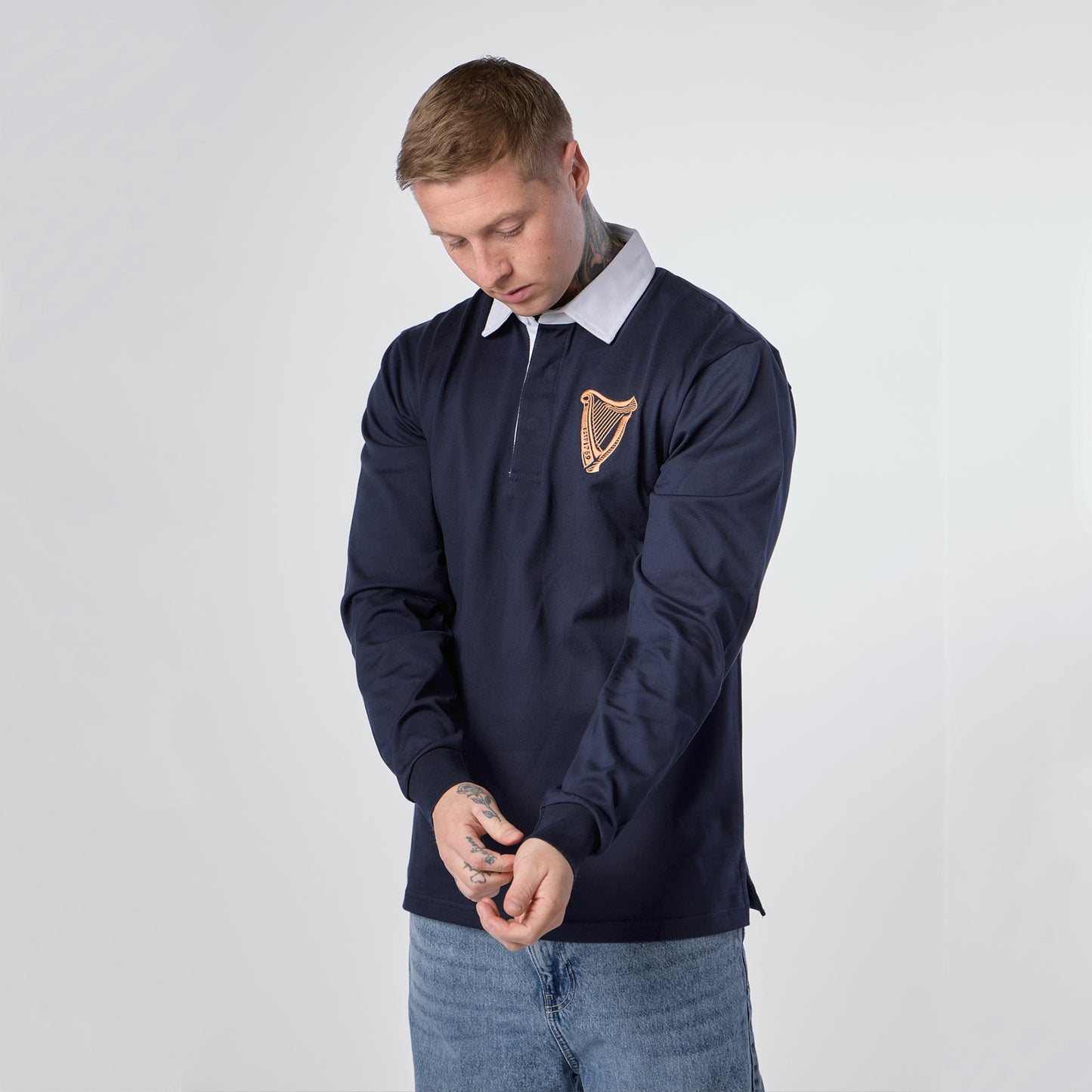 A person wearing the Guinness Navy Traditional Rugby Jersey from Guinness Webstore US, featuring a white collar and a golden harp emblem, looks down as they adjust their cuff.