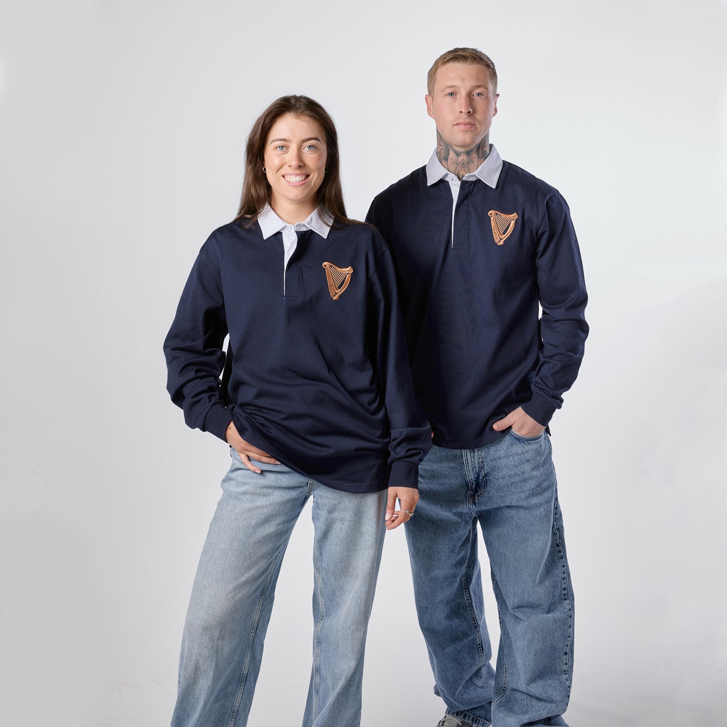 Two people wearing Guinness Navy Traditional Rugby Jerseys from the Guinness Webstore US—with white collars—pair their tops with jeans as they stand side by side against a plain white background.
