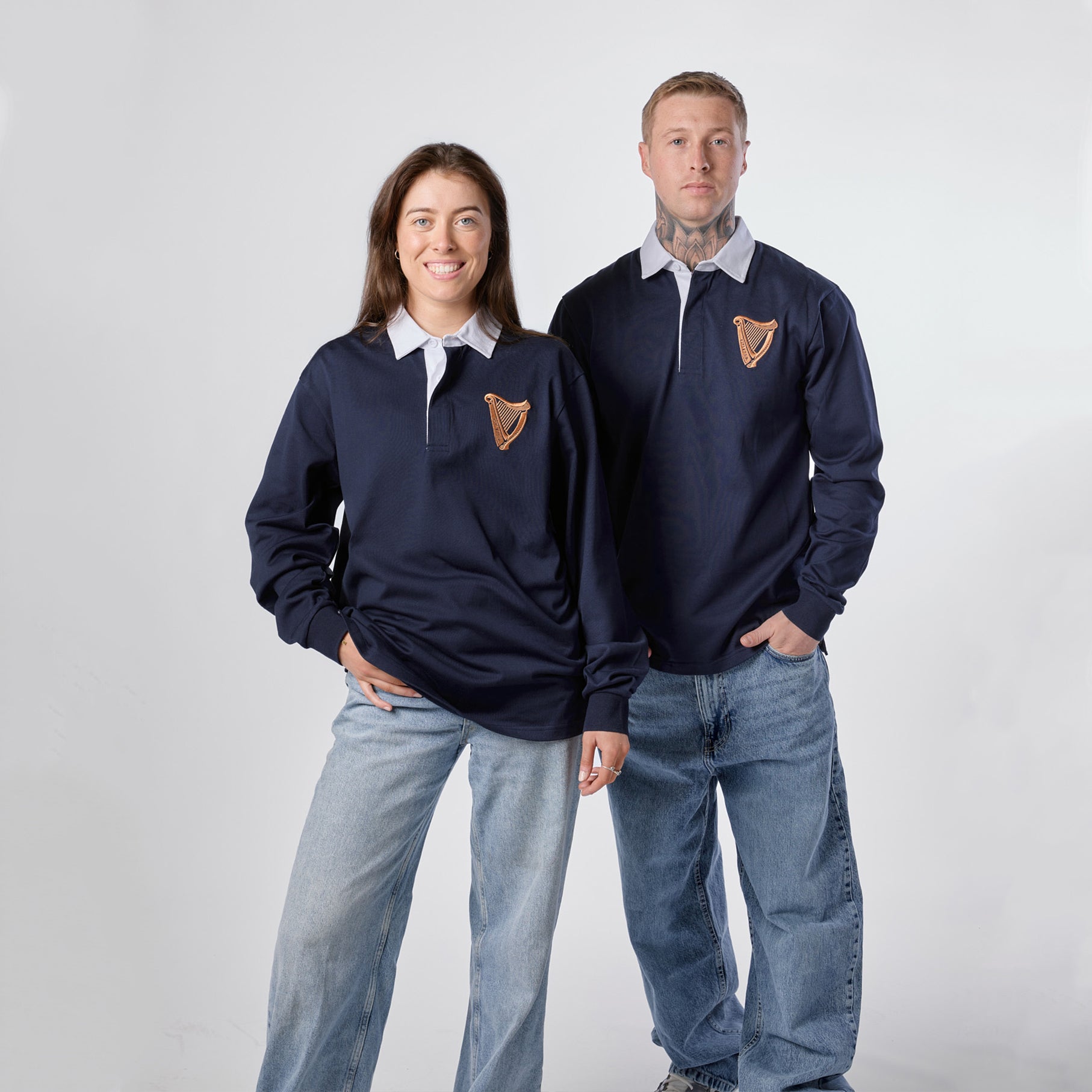 Two people wearing Guinness Navy Traditional Rugby Jerseys from the Guinness Webstore US—with white collars—pair their tops with jeans as they stand side by side against a plain white background.