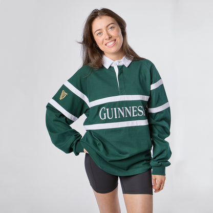 A woman wearing the Guinness Green Traditional Rugby Jersey and black shorts smiles against a plain light background.