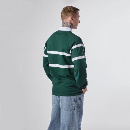 A person with short hair and visible neck tattoos stands with their back to the camera, wearing the Guinness Green Traditional Rugby Jersey by Guinness along with light blue jeans, set against a plain white background.