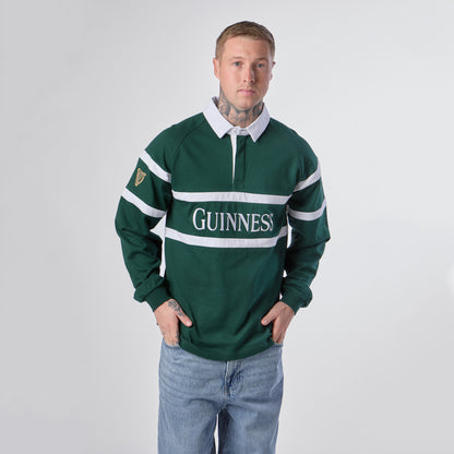 A person wearing the Guinness Green Traditional Rugby Jersey by Guinness, styled like a classic rugby top, and blue jeans stands facing forward against a plain white background.