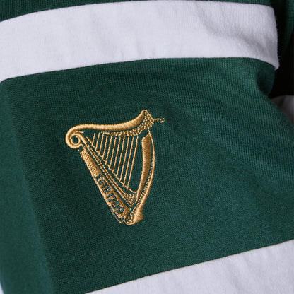 Close-up of the Guinness Green Traditional Rugby Jersey, featuring green and white stripes and a gold embroidered harp emblem—the iconic symbol of Ireland—on the fabric.