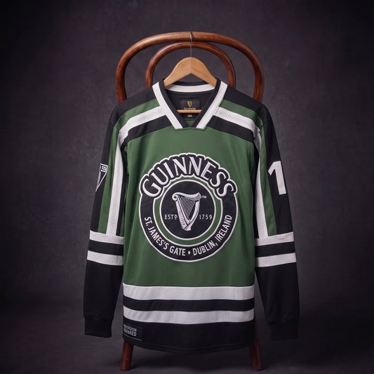 A bold Green & White Hockey Jersey from Guinness, adorned with the iconic logo and harp emblem, hangs on a wooden chair against a dark background.