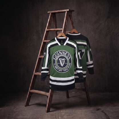 Two Guinness Green & White Hockey Jerseys, each featuring the iconic harp logo, are displayed on a wooden ladder against a dark, textured background.