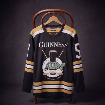 The Guinness Tortoise Hockey Jersey by Guinness Webstore US is displayed on a hanger against a dark background, featuring black and gold colors, the iconic “Guinness” logo, a pint glass, turtle illustration, and the number 5 on the sleeve. Expertly crafted from recycled polyester hockey jersey material.