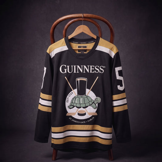 The Guinness Tortoise Hockey Jersey by Guinness Webstore US is displayed on a hanger against a dark background, featuring black and gold colors, the iconic “Guinness” logo, a pint glass, turtle illustration, and the number 5 on the sleeve. Expertly crafted from recycled polyester hockey jersey material.