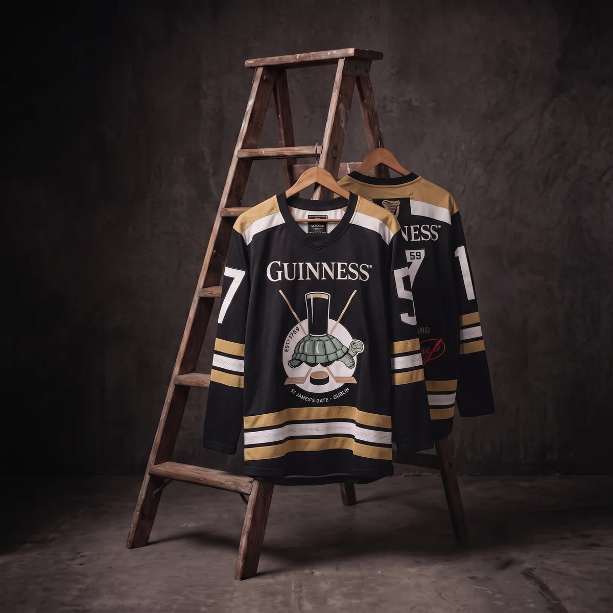 Two Guinness Tortoise Hockey Jerseys by Guinness Webstore US, crafted from recycled polyester in striking black and gold with “Guinness” emblazoned on the front, hang on a wooden ladder against a dark, textured background—a refined display of sustainable Guinness sportswear.