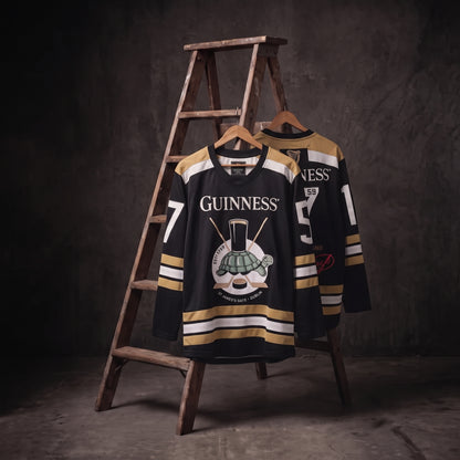 Two Guinness Tortoise Hockey Jerseys by Guinness Webstore US, crafted from recycled polyester in striking black and gold with “Guinness” emblazoned on the front, hang on a wooden ladder against a dark, textured background—a refined display of sustainable Guinness sportswear.