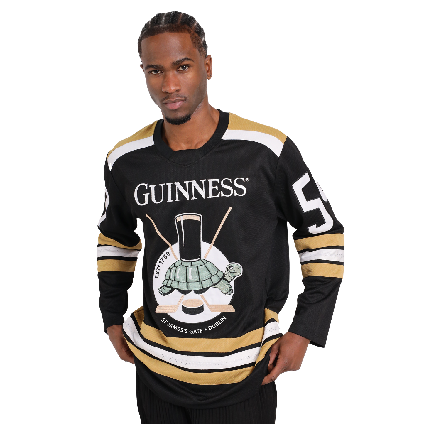 A man stands wearing a black and gold Guinness Tortoise Hockey Jersey with the number 59 on the sleeves. Made from recycled polyester, the front features a turtle carrying a pint of Guinness on its back. The product is available from Guinness Webstore US.