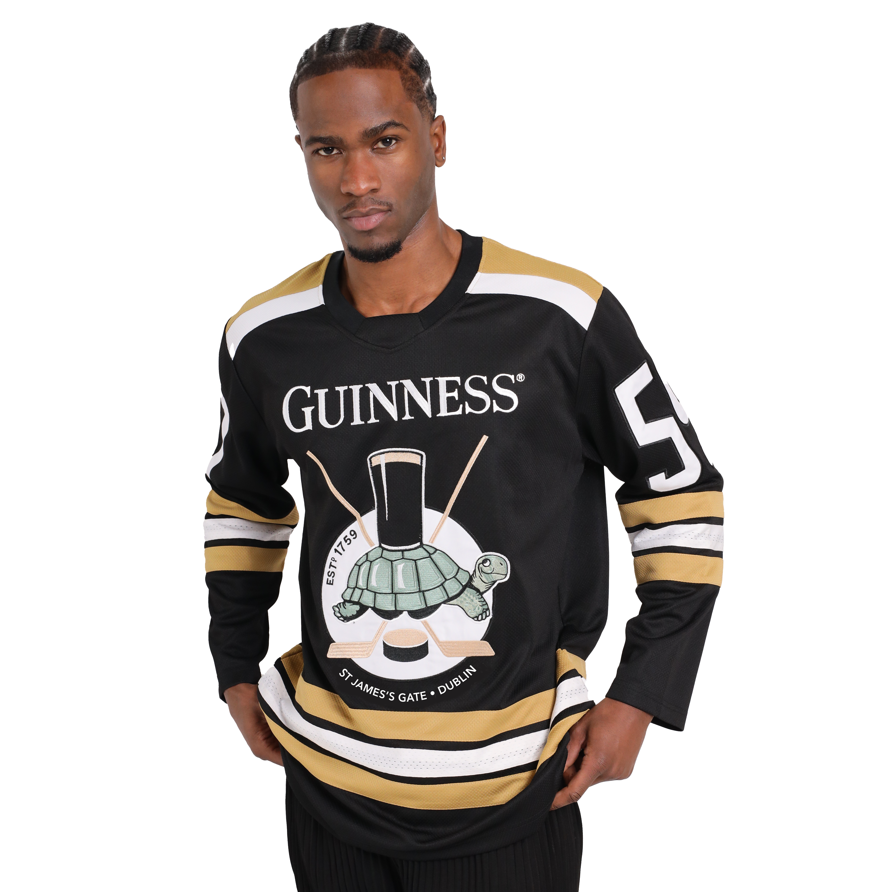 A man stands wearing a black and gold Guinness Tortoise Hockey Jersey with the number 59 on the sleeves. Made from recycled polyester, the front features a turtle carrying a pint of Guinness on its back. The product is available from Guinness Webstore US.