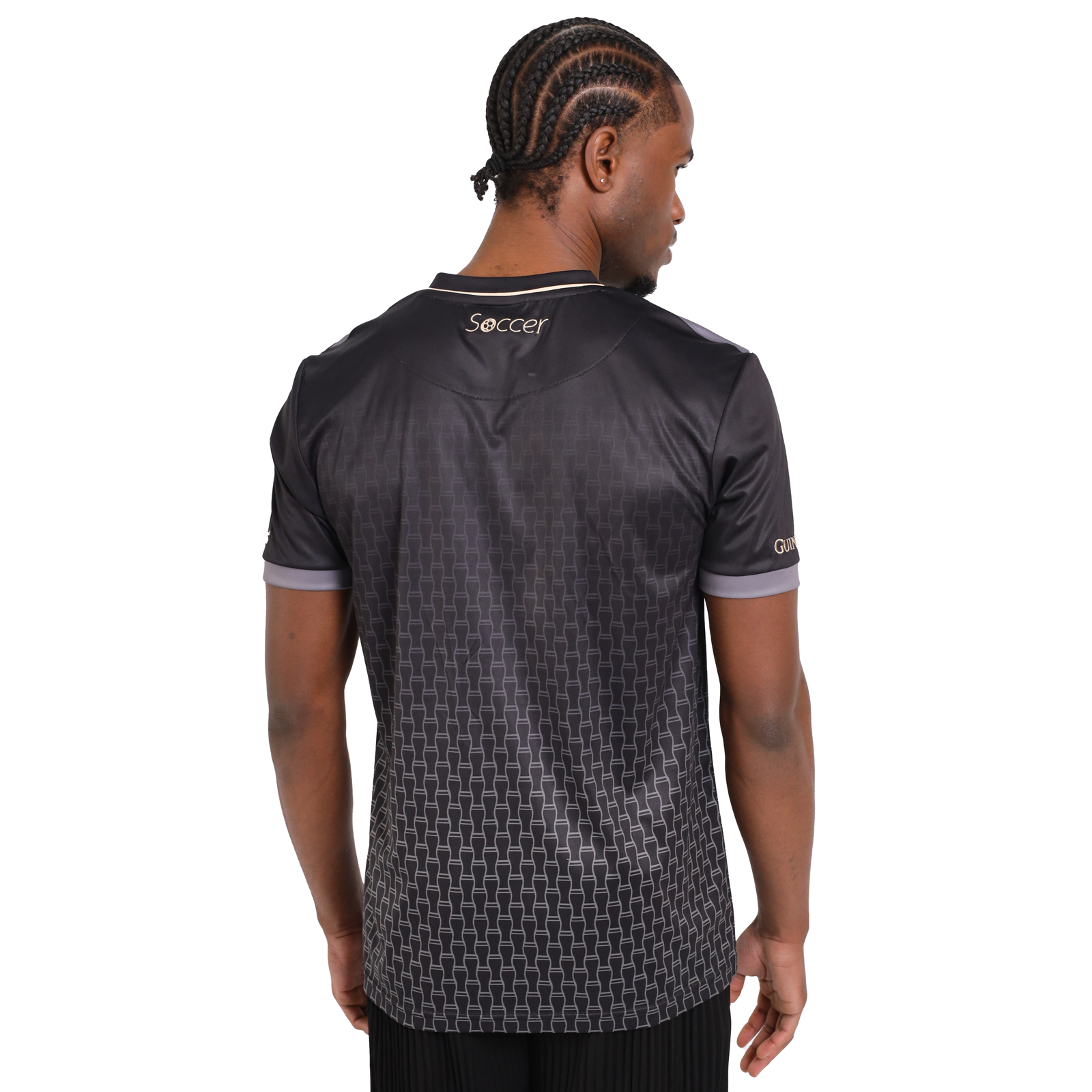 A man stands turned away, showcasing the back of a black Guinness Soccer Jersey with a subtle geometric pattern and the word "Soccer" printed on it, available from Guinness Webstore US.