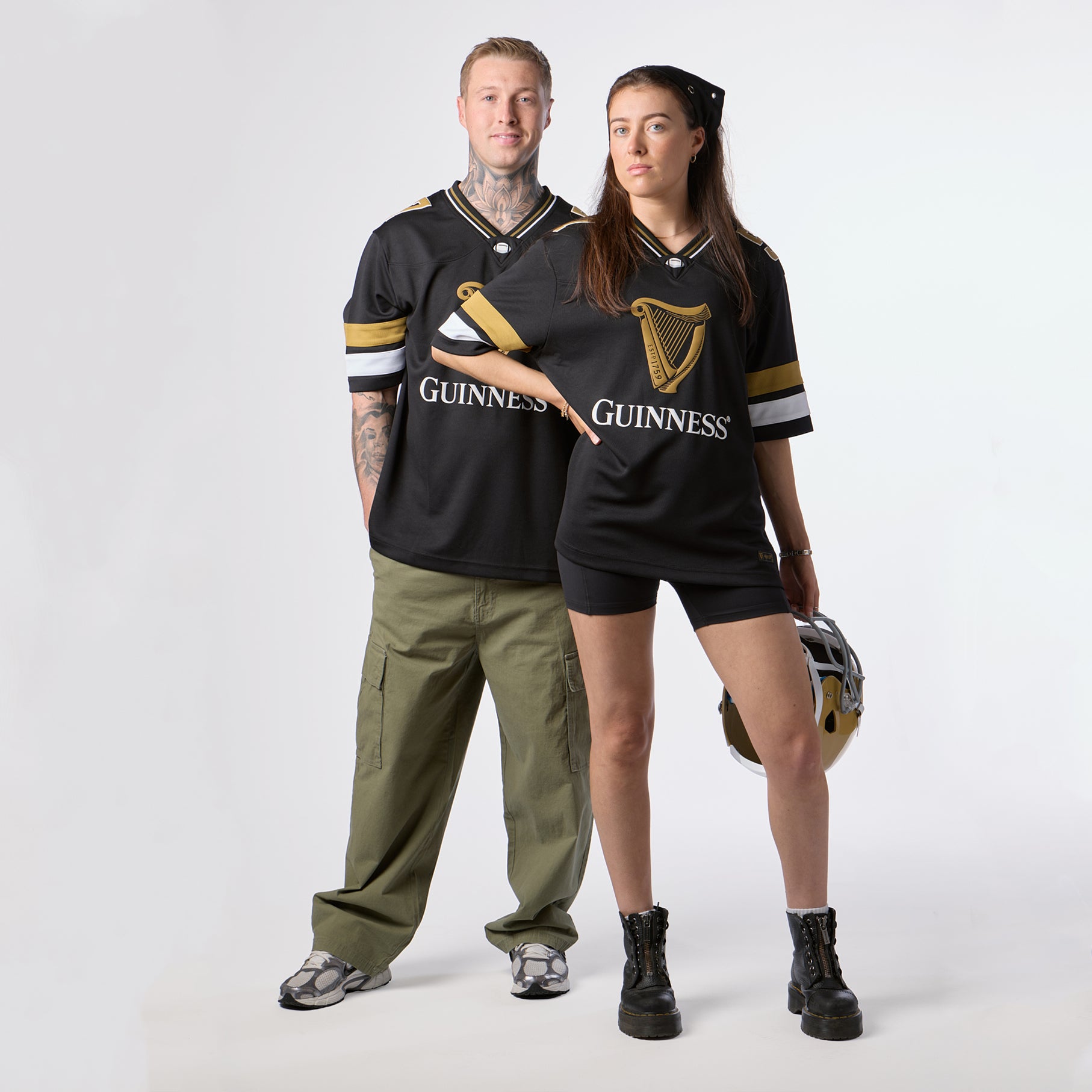 Two individuals wearing matching Guinness Webstore US Black American Football Jerseys pose against a white background; one holds an American football helmet, while the other stands with hands behind their back, showcasing stylish Guinness Webstore US apparel.
