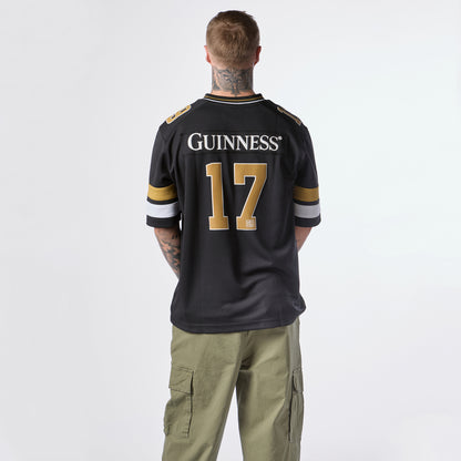 A person with tattoos is seen from behind wearing the Guinness Black American Football Jersey by Guinness Webstore US, featuring “GUINNESS” and the number 17, paired with green cargo pants.