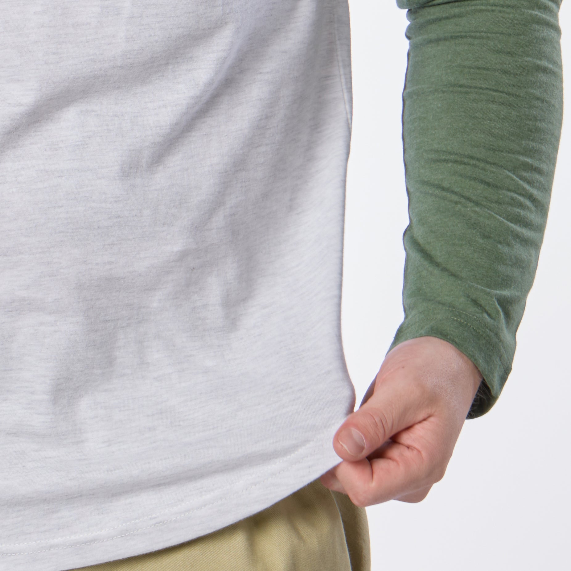 A person wearing the Guinness Baseball T-Shirt—a light gray shirt with green raglan sleeves—holds the bottom edge of their shirt with one hand.