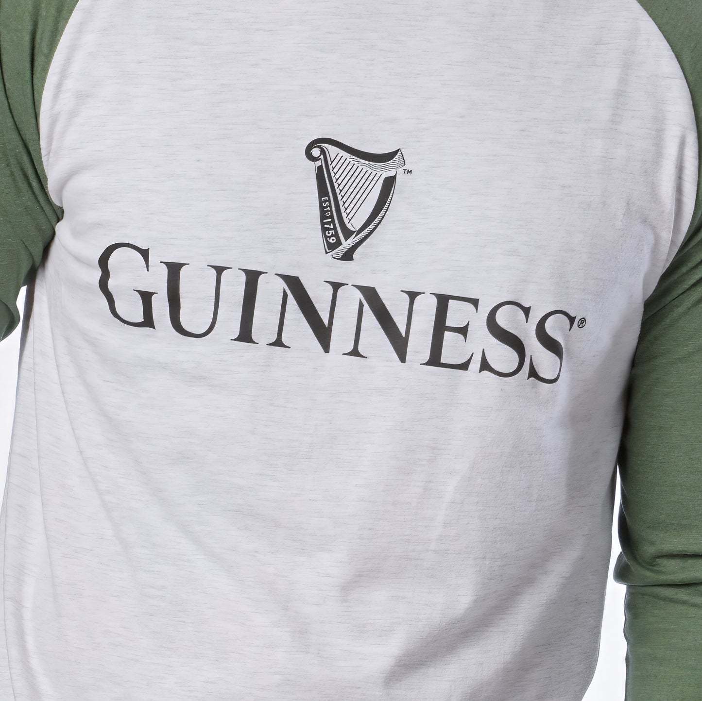 A person is wearing the Guinness Baseball T-Shirt by Guinness, featuring white and green raglan sleeves with the classic Guinness logo and harp symbol on the chest. Crafted from soft heathered jersey cotton, this shirt offers all-day comfort.