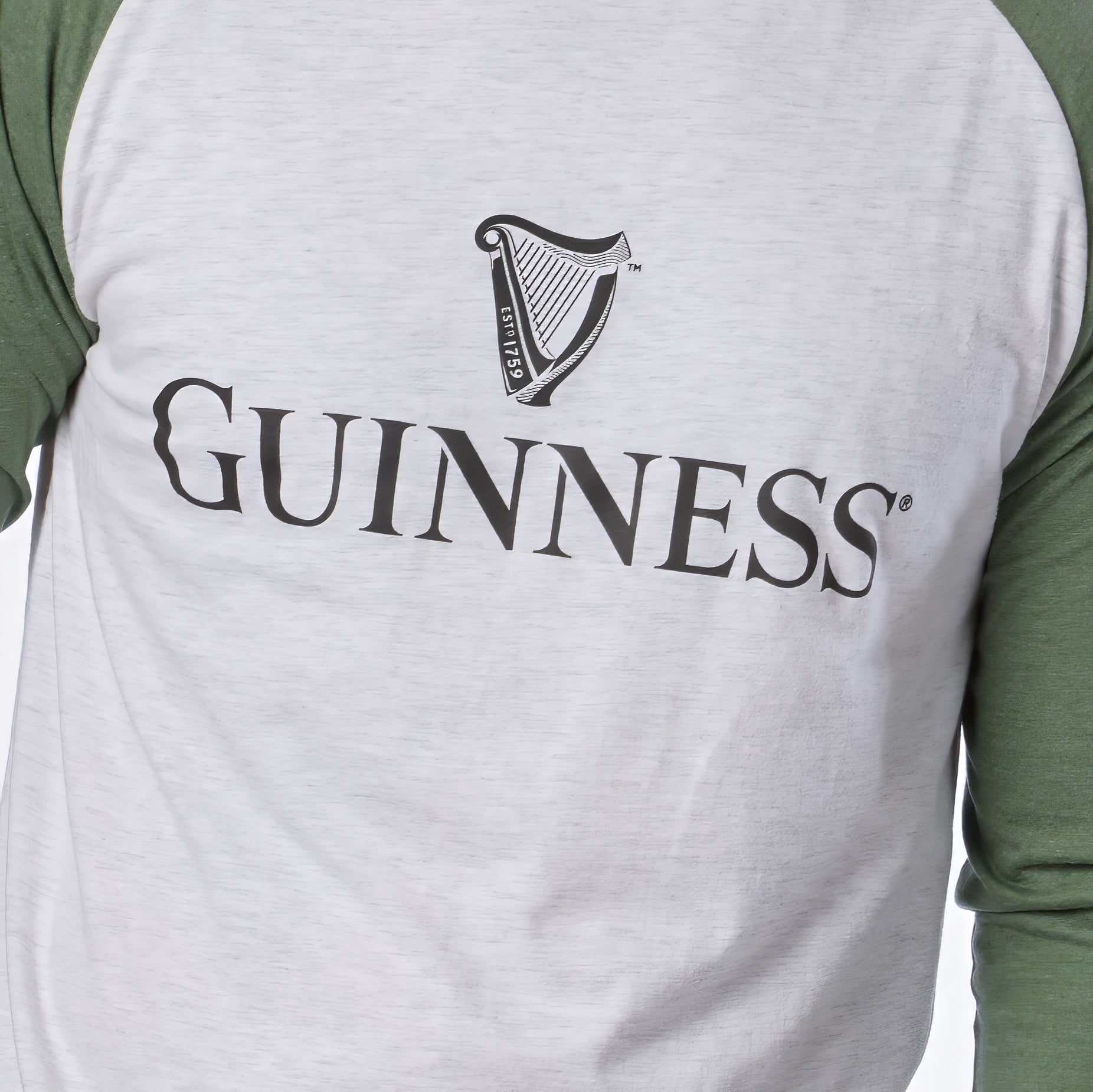 A person is wearing the Guinness Baseball T-Shirt by Guinness, featuring white and green raglan sleeves with the classic Guinness logo and harp symbol on the chest. Crafted from soft heathered jersey cotton, this shirt offers all-day comfort.