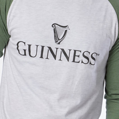 A person is wearing the Guinness Baseball T-Shirt by Guinness, featuring white and green raglan sleeves with the classic Guinness logo and harp symbol on the chest. Crafted from soft heathered jersey cotton, this shirt offers all-day comfort.