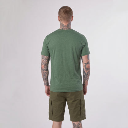 A man with tattoos stands facing away, wearing a green Guinness Vintage Harp Tee by Guinness and olive cargo shorts against a plain light background.