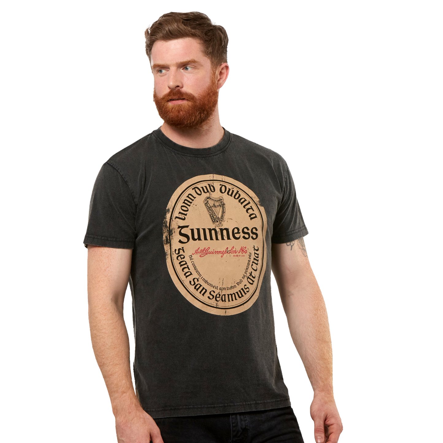 A man with a red beard wears the Guinness Black Distressed Label Tee, a unisex shirt featuring a large vintage-style graphic on the front.