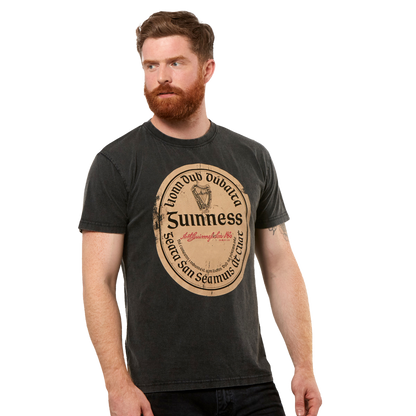 A man with a red beard wears the Guinness Black Distressed Label Tee, a unisex shirt featuring a large vintage-style graphic on the front.
