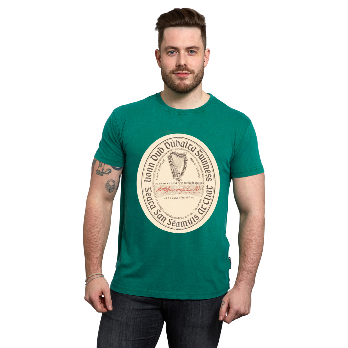 A man wearing a green short-sleeved Guinness Green Label Premium Tee with an oval graphic featuring a harp and text on the chest.