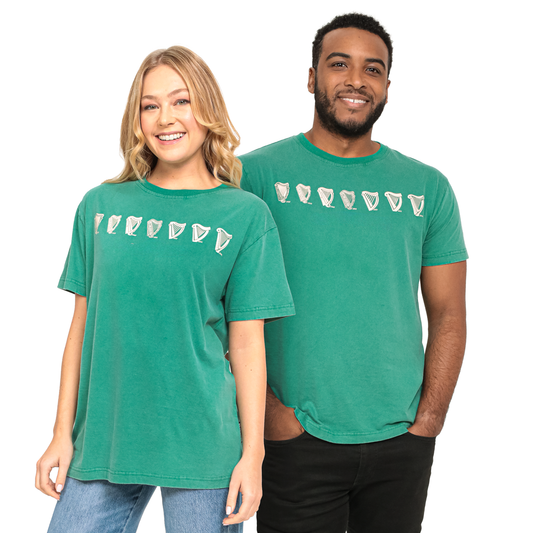 Two people, one woman and one man, wearing matching green T-shirts with a design featuring multiple white seashells, stand side by side and smile. Their outfits highlight the comfort of 100% cotton fabric while showcasing the charm of a Guinness Green Evolution Harp Tee.