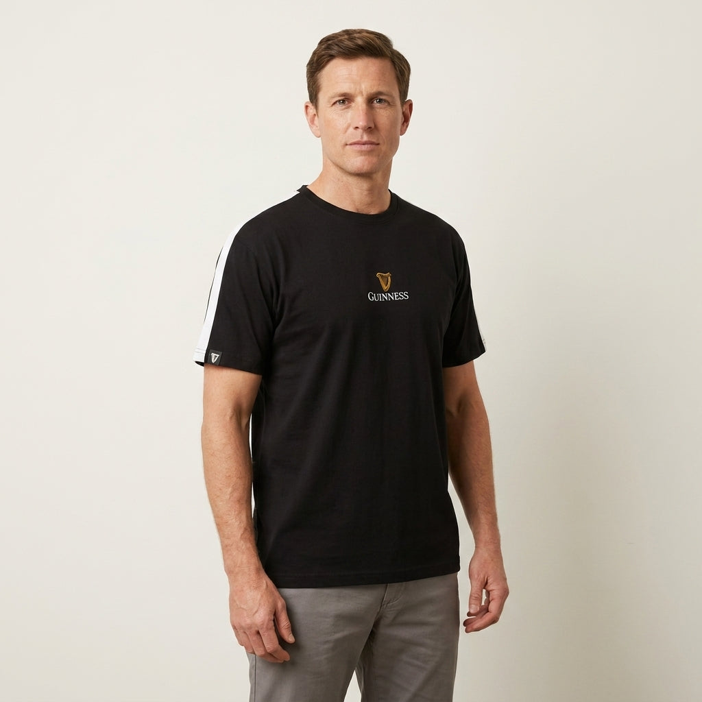 A man in a Guinness Webstore US Toucan Soccer Black Tee stands against a light background, capturing the playful spirit of the classic "My Goodness My Guinness" campaigns.