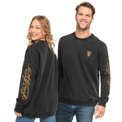 A man and a woman wear the black Guinness Gold Harp & Signature Distressed Sweatshirt featuring vintage-inspired gold harp and script graphics on the chest and sleeves.