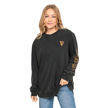A person wearing a black Guinness Gold Harp & Signature Distressed Sweatshirt with a small gold harp logo on the chest and gold script on the left sleeve.