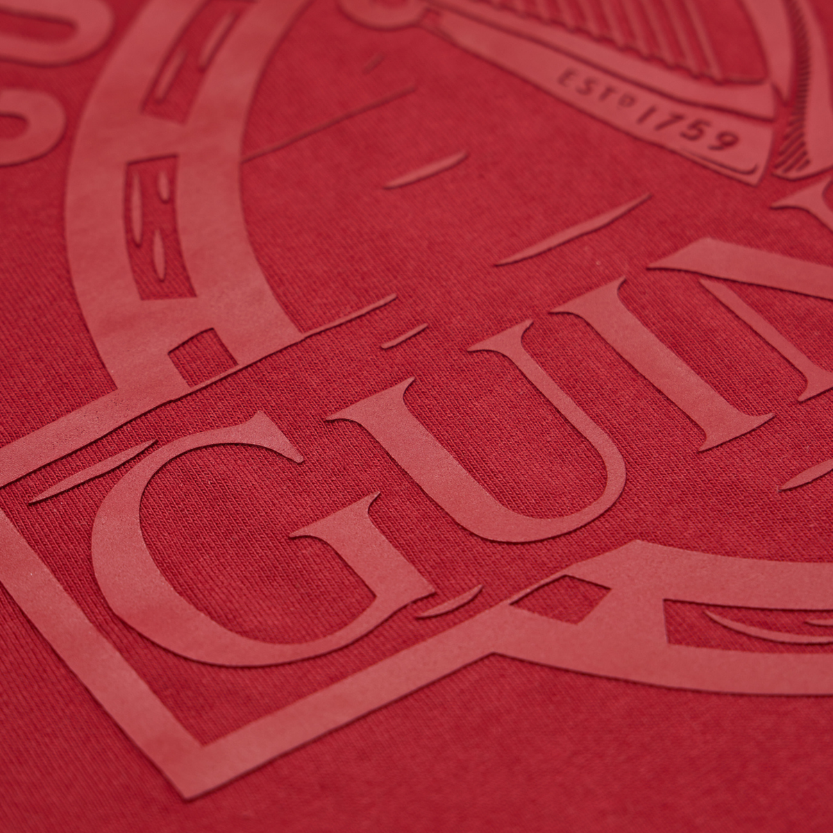 Close-up of the textured surface of the Guinness Cooperage Burnt Red Heavyweight Tee by Guinness Webstore US, showing a partially embossed “GUIN” from the iconic logo.