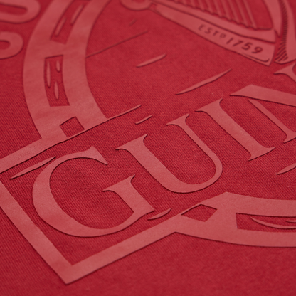 Close-up of the textured surface of the Guinness Cooperage Burnt Red Heavyweight Tee by Guinness Webstore US, showing a partially embossed “GUIN” from the iconic logo.
