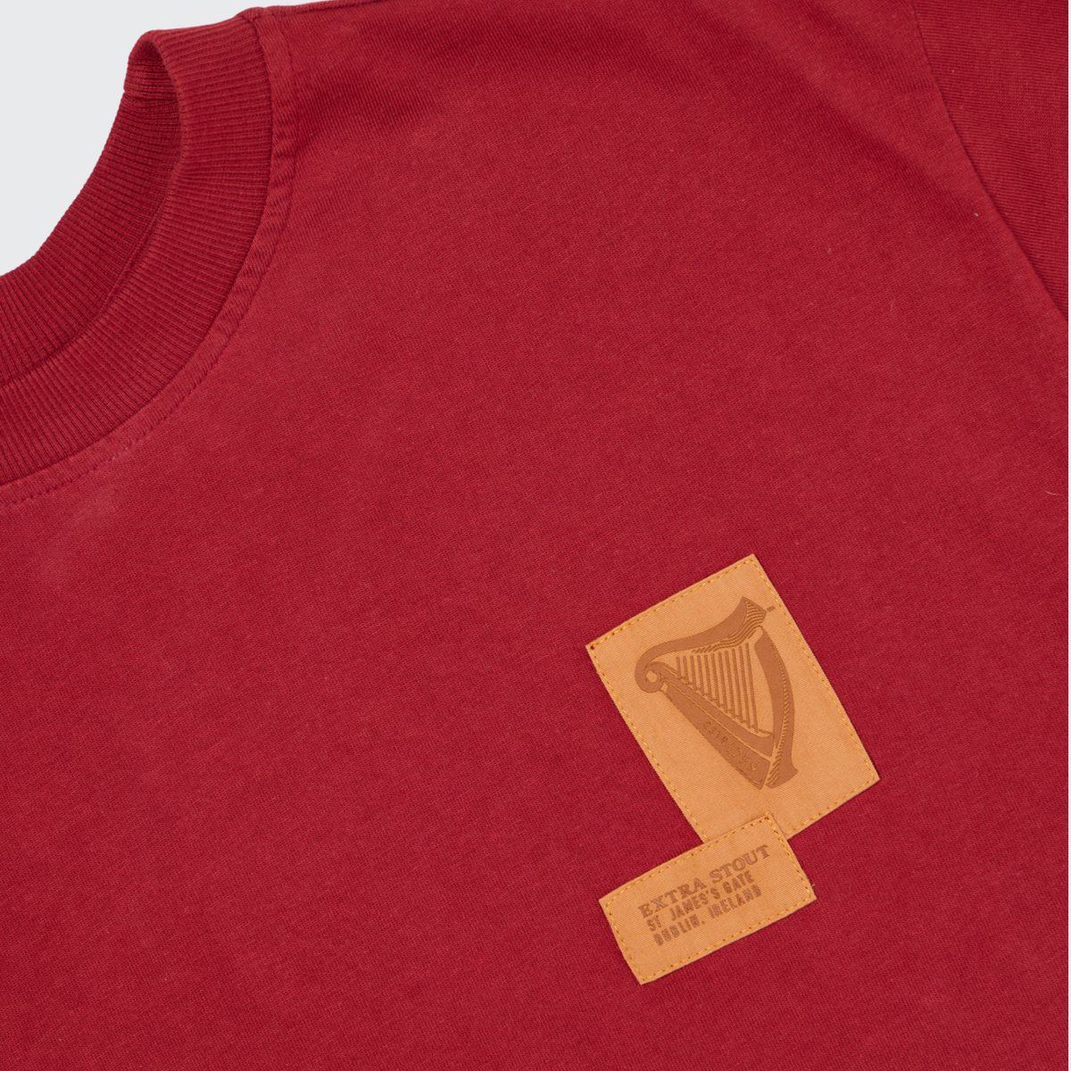 A close-up of the Guinness Cooperage Burnt Red Heavyweight Tee from Guinness Webstore US, featuring a distinctive brown patch with a harp design and subtle printed text on the front, inspired by classic cooperage styling.