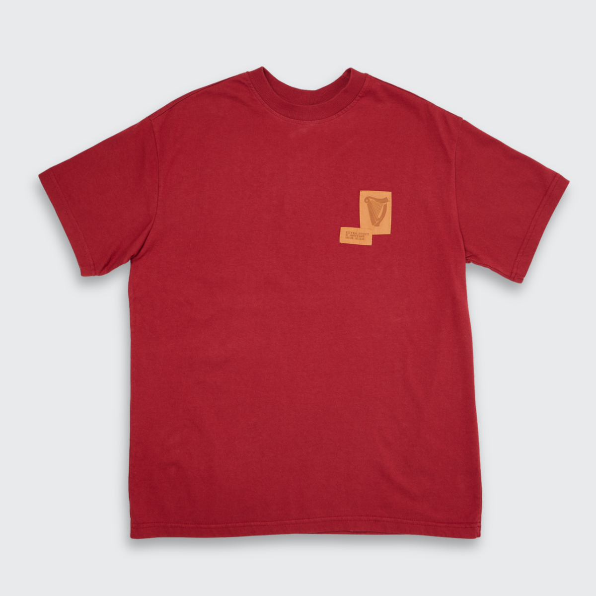 Introducing the Guinness Cooperage Burnt Red Heavyweight Tee from Guinness Webstore US—a burnt red t-shirt featuring a small tan patch and an embroidered harp design on the left chest, inspired by the craftsmanship of the legendary Guinness cooperage.