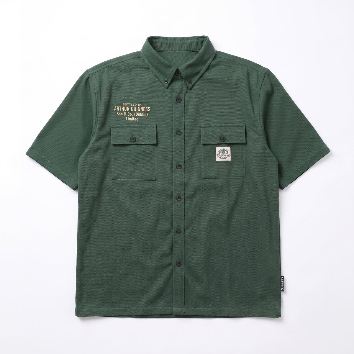 The Guinness Cooperage Work Shirt is a forest green, short-sleeve, heavyweight cotton button-up with two chest pockets, embroidered text left, and logo patch right.