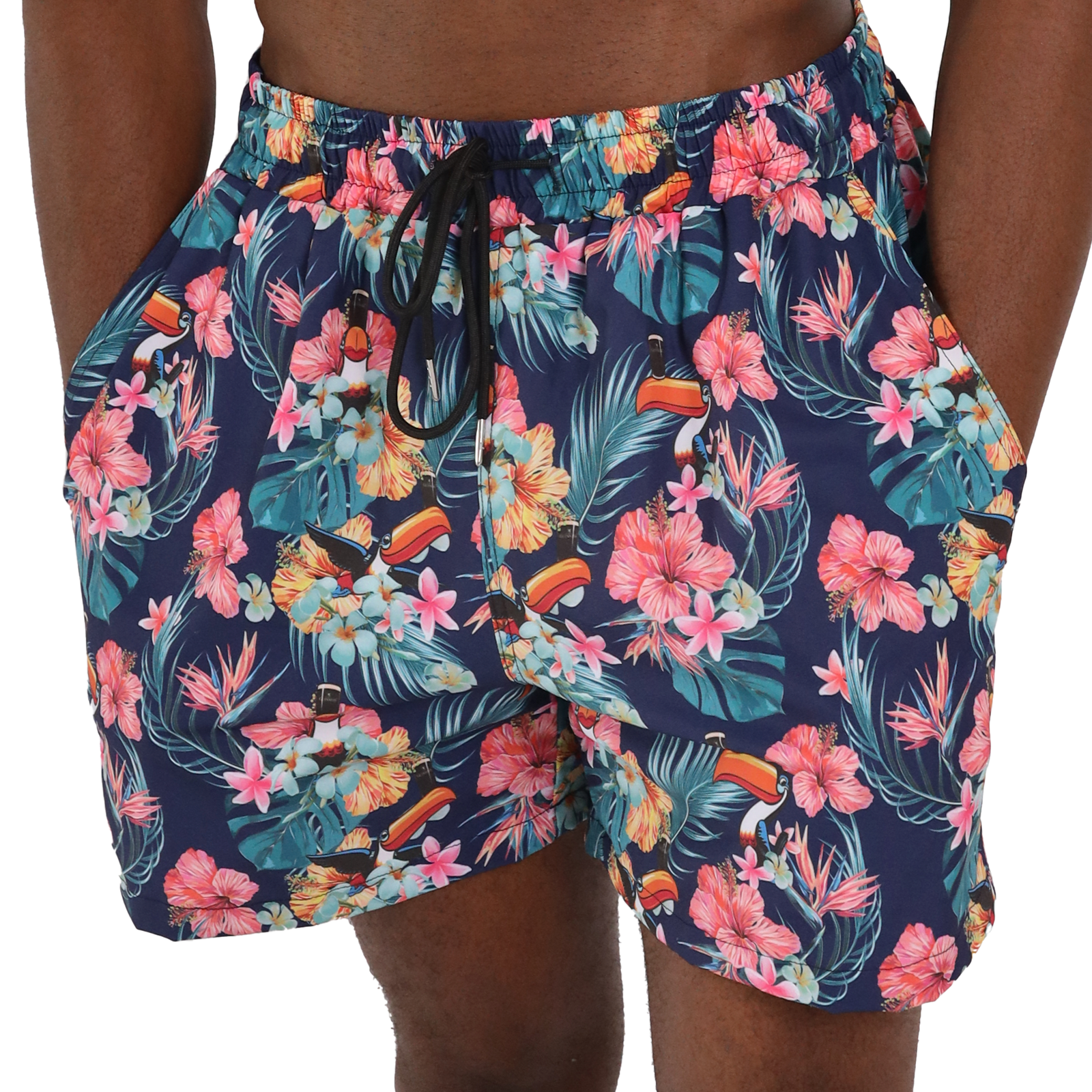 A person wearing Guinness Toucan Hawaiian Beach Shorts from Guinness Webstore US, with a colorful floral and leaf pattern, featuring pink and yellow flowers, and tropical motifs, exuding a tropical flair, with hands in pockets.