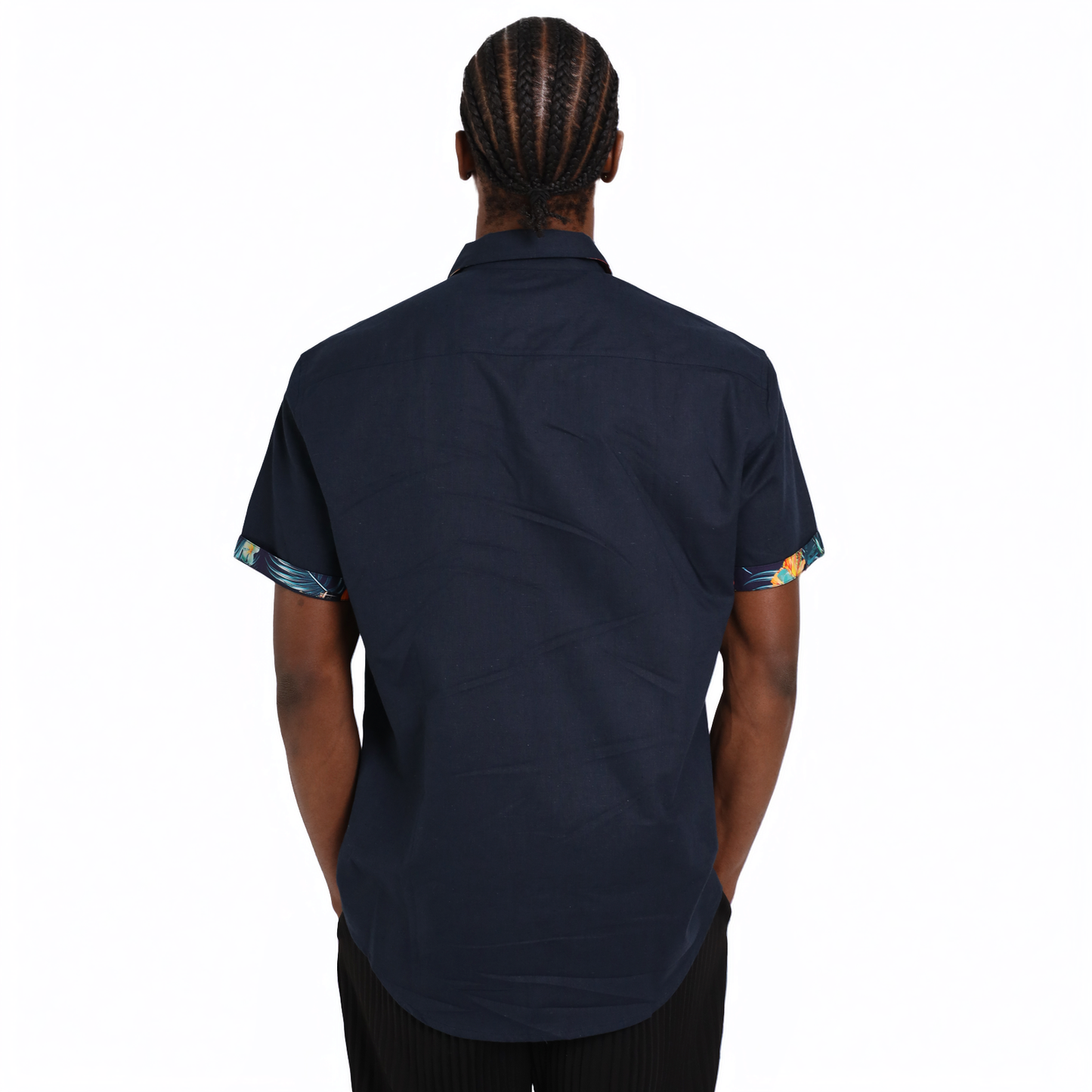A person with braided hair is seen from the back wearing a short-sleeved Guinness Navy Linen Summer Shirt by Guinness Webstore US, featuring patterned sleeve cuffs, against a plain white background.
