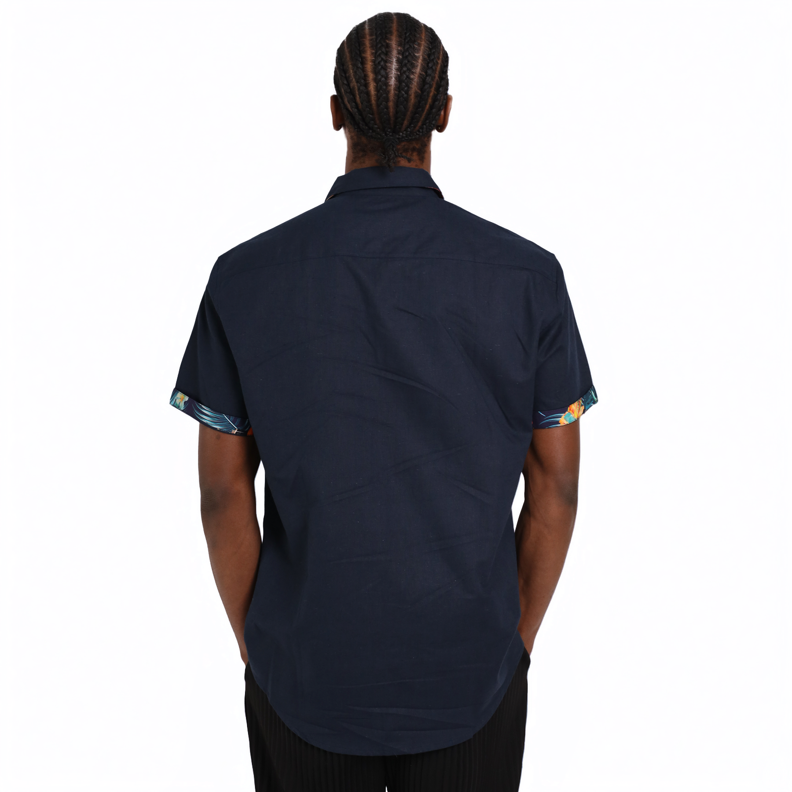 A person with braided hair is seen from the back wearing a short-sleeved Guinness Navy Linen Summer Shirt by Guinness Webstore US, featuring patterned sleeve cuffs, against a plain white background.