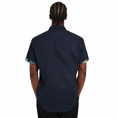 A person with braided hair is seen from the back wearing a short-sleeved Guinness Navy Linen Summer Shirt by Guinness Webstore US, featuring patterned sleeve cuffs, against a plain white background.