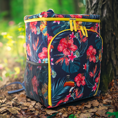 The Guinness Toucan Hawaiian Cooler Bag, featuring a floral pattern and yellow zippers, is nestled against a tree on a forest floor covered with dry leaves—a perfect outdoor accessory available from Guinness Webstore US.