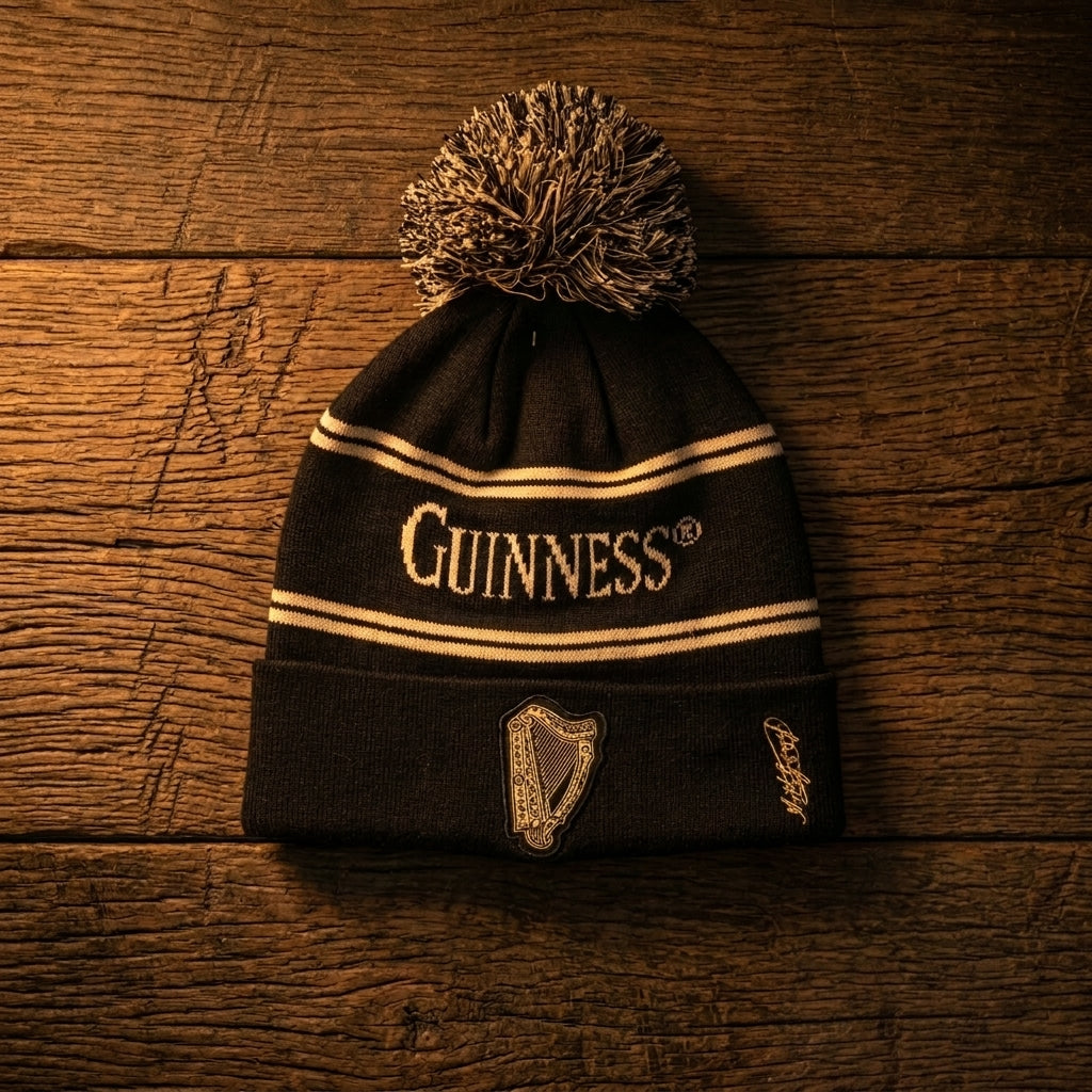 The Guinness Black & Gold Sports Beanie – Vintage Harp Knit, featuring the classic harp logo, is displayed on a wooden surface.