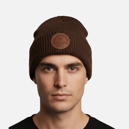 A man wears a Guinness Cooperage Brown Knitted Beanie with a round leather patch, facing the camera against a plain white background.