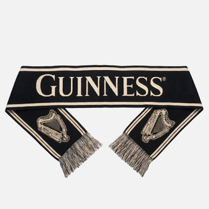 The Guinness Black & Gold Sports Scarf – Vintage Harp Knit features bold white "Guinness" lettering and classic harp designs at each fringed end—a perfect sports scarf for Guinness fans.