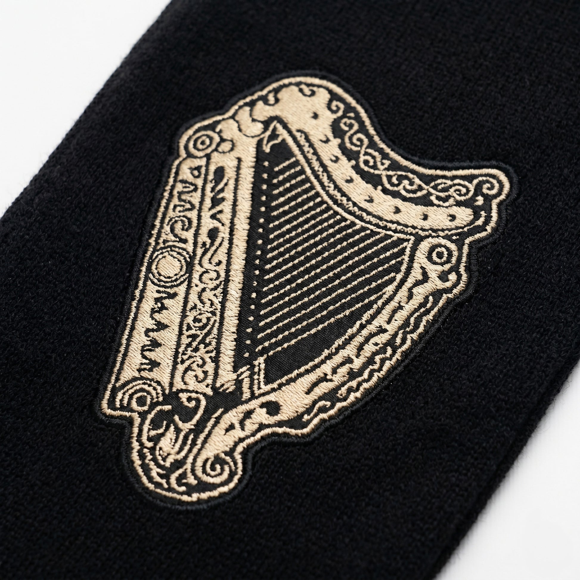 The Guinness Black & Gold Sports Scarf – Vintage Harp Knit features a gold embroidered vintage harp on black fabric with ornate edge detailing—a bold accessory for fans of classic Guinness style.