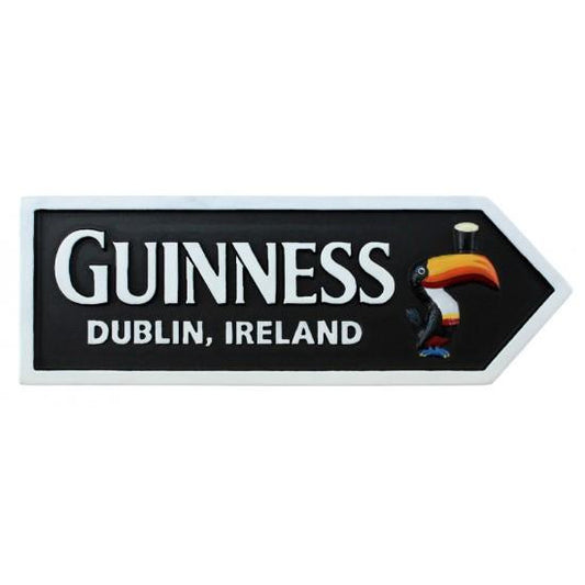 The Guinness Resin Magnet – Road Sign from Guinness Webstore US features "Guinness Dublin, Ireland" and a toucan with a pint on its beak, set on a black background with a white arrow border—an ideal Irish souvenir.